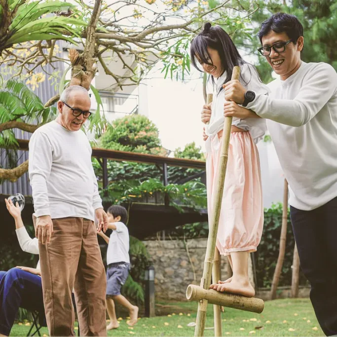 Ông và cháu chơi đi cà kheo trong vườn cùng người nhà